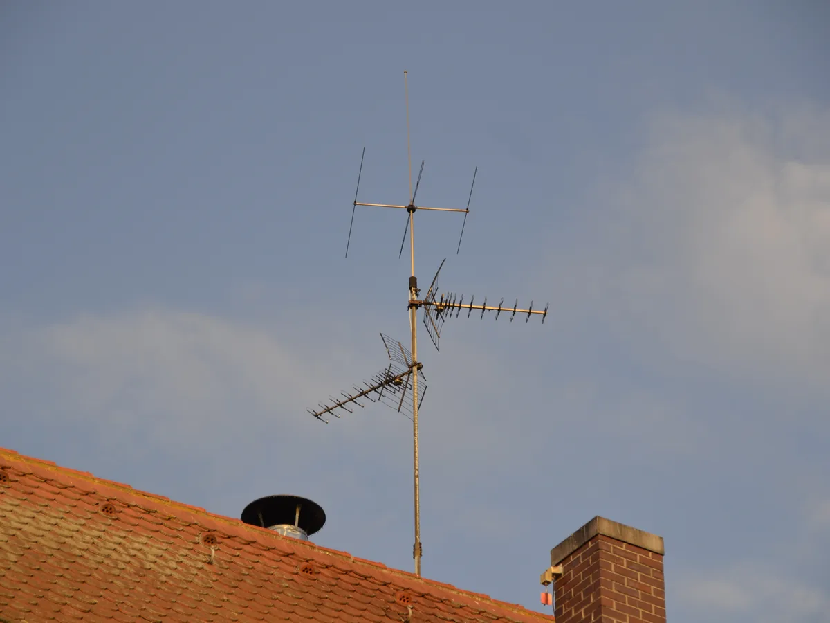 A roof-mounted TV antenna above a tiled roof against a blue sky