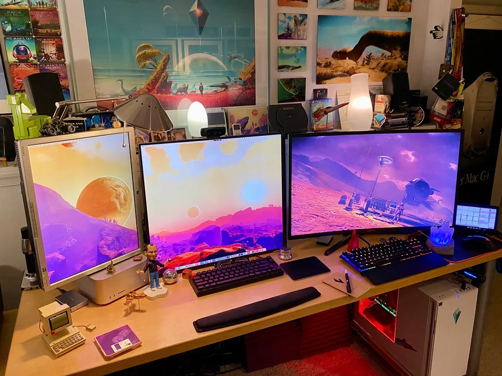 A PC gaming desk with three monitors, keyboards and a lit tower PC