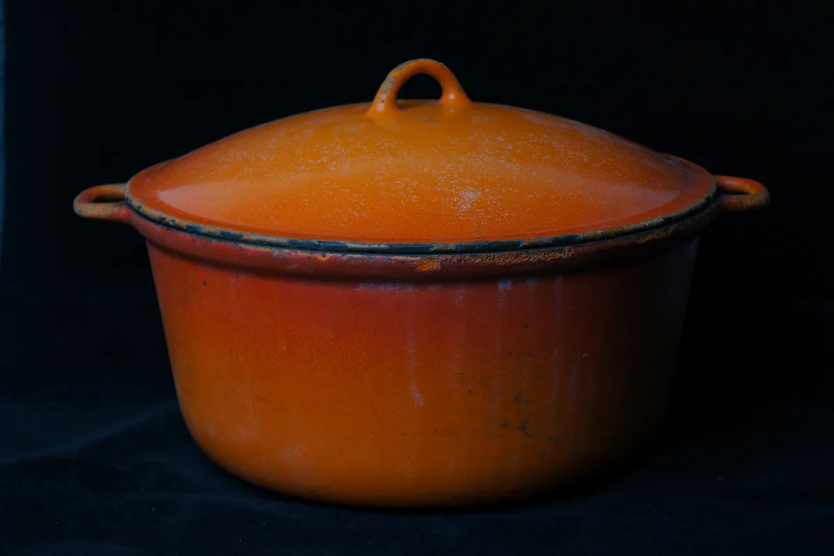 Amazon Basics Enameled Cast Iron Dutch Oven, 4.3-Quart (Blue): stock photo (An orange enameled cast iron pot with lid on a dark background), not the actual product