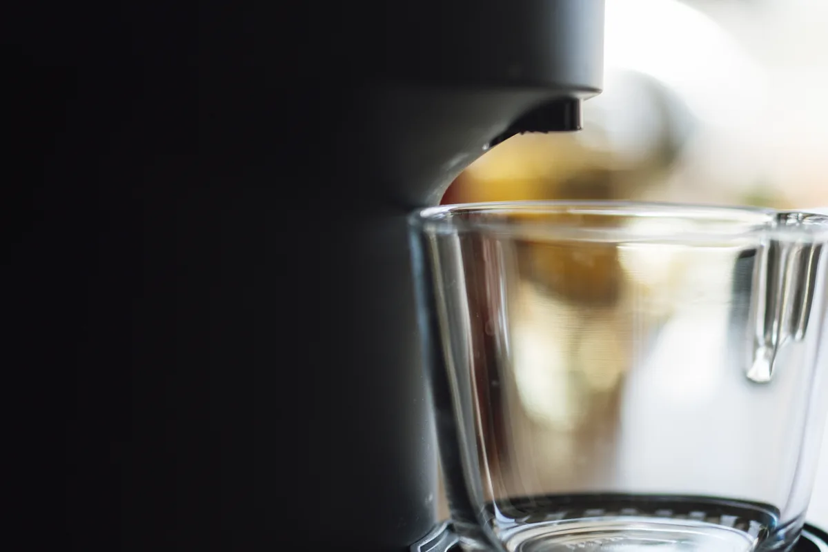 Keurig K-Elite Single-Serve K-Cup Pod Coffee Maker, Brushed Slate: stock photo (Stock photo, not the actual product: the spout of a dark single-serve coffee machine above a clear glass cup), not the actual product