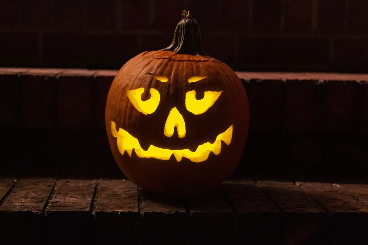 Hershey's Assorted Chocolate Halloween Candy Bulk Variety Pack, 80.39 oz (265 pieces): stock photo (A carved, glowing jack-o'-lantern on a brick ledge at night), not the actual product